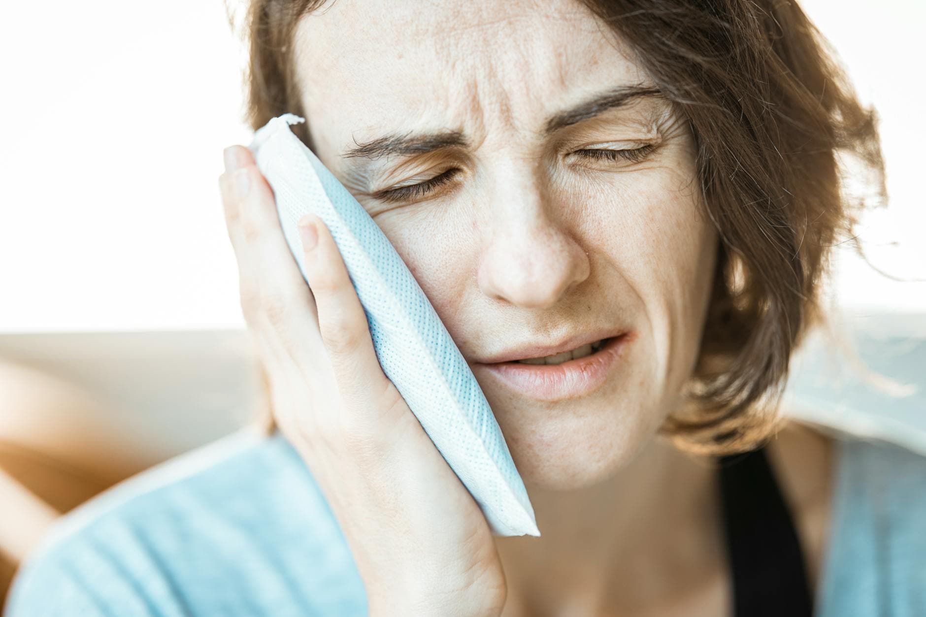 Woman holding a cold compress against her cheek, finding relief from jaw pain